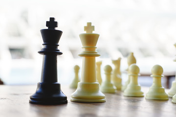 Black and white chess kings faced between defocused pieces on wooden board.