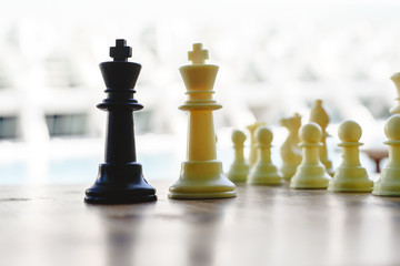 Black and white chess kings faced between defocused pieces on wooden board.
