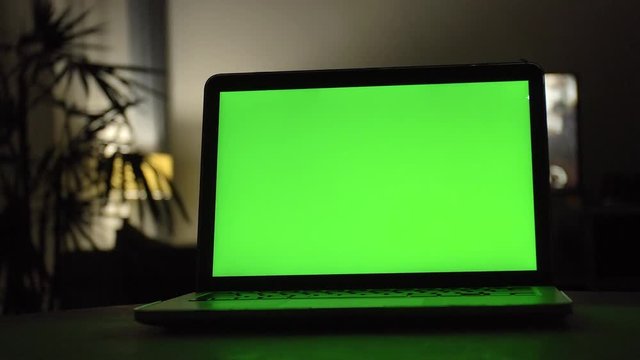 Laptop with green screen. Dark home office . Dolly shot of Perfect to put your own image or video. 