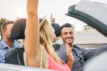Happy friends having fun in convertible car at sunset in vacation - Young rich people making party and dancing in auto cabriolet during their road trip - Friendship, travel, youth lifestyle concept - obrazy, fototapety, plakaty
