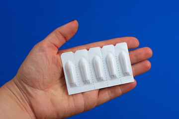 Medical Suppository, Rectal or Vaginal in the hands of a woman. Isolated on blue Background.