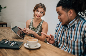 Two young creatives looking serious while pointing at a tablet ina boardroom