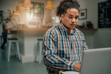 Handsome mixed race guy working on laptop ina coffee cafe