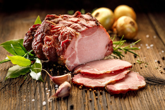 Sliced smoked gammon on a wooden  table with addition of fresh  herbs and aromatic spices.   Natural product from organic farm, produced by traditional methods