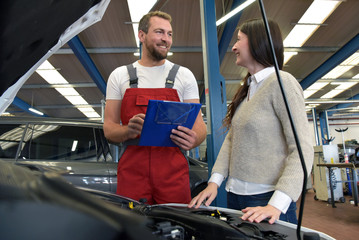 Kundendienst in der Autowerkstatt - Mechaniker und Kundin besprechen Service am PKW // Customer...