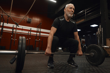 Handsome bearded Caucasian male pensioner with strong muscled arms holding barbell, ready to do...