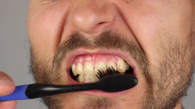man with beard and mustache thoroughly brushes his teeth with black toothbrush without toothpaste, movements from side to side, gum massage, front view, closeup