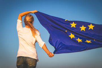 EU flag in female hands. Woman holding waving European Union flag against blue sky - obrazy, fototapety, plakaty