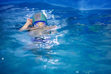 Fototapeta na wymiar Boy in a hat and swimming goggles is learning to swim in a pool.