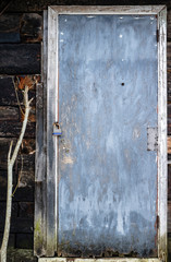 Old rotten door to the barn with a padlock in the countryside. Close-up.