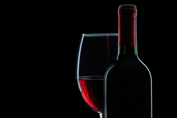 bottle and wineglass with red wine on black background close up view.