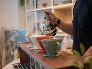 drip coffee, hand of a man is pouring hot water slowly on crushed coffee beans on paper filter lining in a funnel