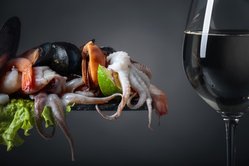 Mixed raw delicious seafood with lime slices and glass of white wine.
