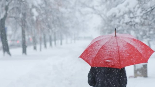 Woman with red umbrella in snow enjoying the first snowfall of the winter season