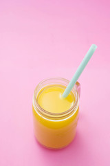 Colorful composition with mason jar glass full of fresh orange juice with straw, fruit, isolated on pink background. Close up, copy space, top view.