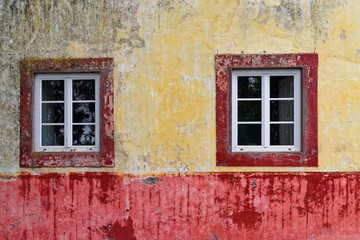 Fototapeta na wymiar Two windows on an old and dirty wall of colorful house facade