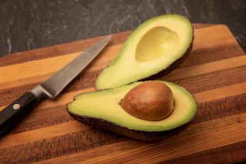 Avocado cut in half on a wooden chopping boars with a knife 
