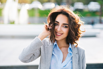 Closeup portrait of cute brunette girl with short hair posing in city.  She wears blue shirt, gray...