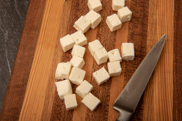 Cubed Feta cheese on a wooden chopping board with a knife