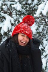 portrait of young smiling woman in winter clothes in red hat with bubo fir tree in background