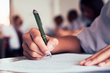 Close-up to student holding pen and writing final exam in examination room or study in...