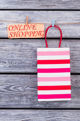 Obraz premium Striped shopping bag on wooden background. Paper gift bag hanging on clothesline with clothespins. Save your time and money.