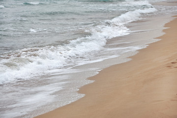 Water washing sand on the beach on overcast day. Detail on small white waves forming. Abstract sea background.