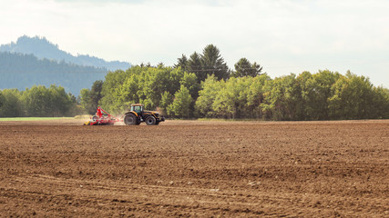 Tractor sowing in empty field on countryside, small trees in background.