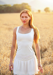Fototapeta na wymiar Young woman in white dress, sun back light wheat field in background.
