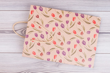 Brown paper shopping bag with flowers pattern. Kraft paper gift bag with colorful tulips printing on wooden background. Floral design gift bag.