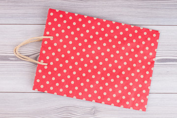 Red polka dot paper shopping bag. Kraft paper dotted gift bag on gray wooden background.