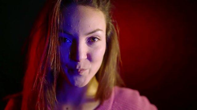 portrait of cute Asian girl with pimples on her face in neon light in dark room looking at camera and smiling
