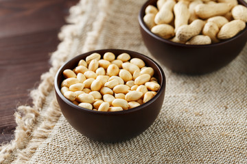 Peanuts in the shell and peeled close-up in cups. Roasted peanuts in their shells and peeled against a brown cloth.