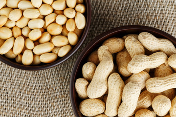 Peanuts in the shell and peeled close-up in cups. Roasted peanuts in their shells and peeled against a brown cloth.