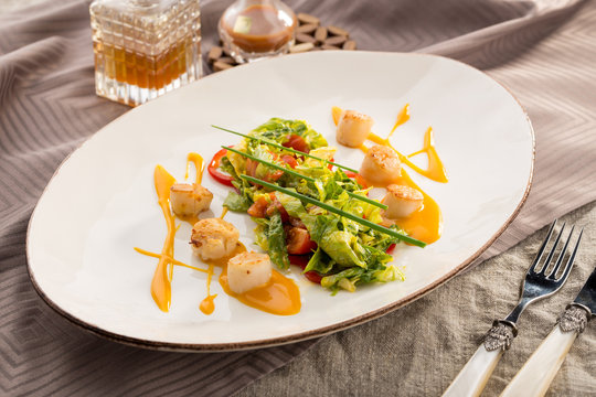 healthy and tasty seafood salad with fried scallops on white plate on grey table