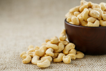 Cashew nuts in a wooden bowl on a burlap cloth background.