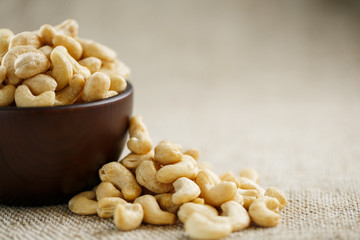 Cashew nuts in a wooden bowl on a burlap cloth background.