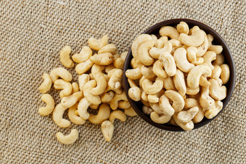 Cashew nuts in a wooden bowl on a burlap cloth background.