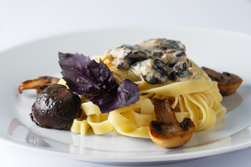Pasta tagliatelle with creamy alfredo mushroom sauce on a white plate. Leaf of a basil. Close up. Selective focus.