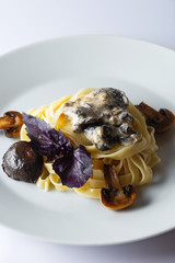Pasta tagliatelle with creamy alfredo mushroom sauce on a white plate. Leaf of a basil. Close up. Selective focus.