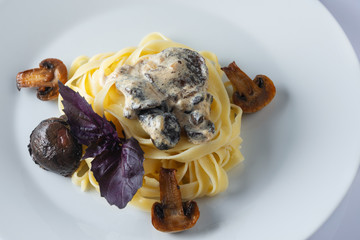 Pasta tagliatelle with creamy alfredo mushroom sauce on a white plate. Leaf of a basil. Close up. Selective focus.