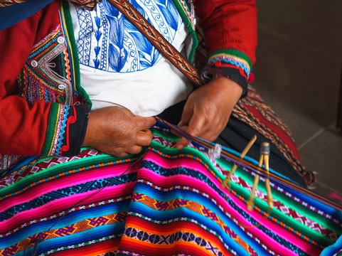 Hands of peruvian woman making alpaca wool carpet with national pattern close-up. Manufacture of wool material in Peru, Cusco. Woman dressed in colorful traditional native Peruvian closing
