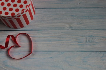 Fototapeta na wymiar Коробка и красная лента в виде сердца , на сером деревянном фоне. 