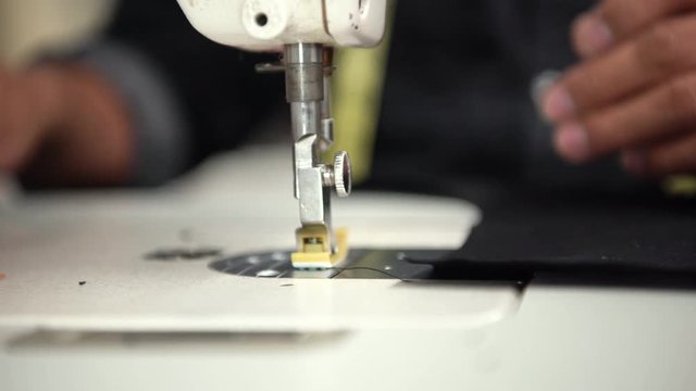 Close up seamstress using sewing machine stiching fabric together to create clothing.