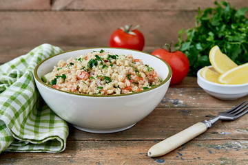 Fresh healthy salad with quinoa, tomatoes, cucumber and parsley on wooden background. Healthy, diet, vegetarian food concept. Flat lay