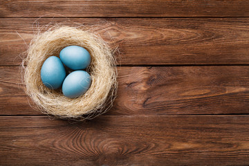 Three blue Easter eggs painted by hibiscus, in a nest with feathers on a wooden background. Easter symbol. Copy space