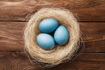 Three blue Easter eggs painted by hibiscus, in a nest with feathers on a wooden background. Easter symbol. Copy space