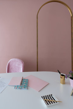 Cozy Pink Working Corner With Antique Gold Arch Frame Inthe Background And White Working Top With Pink Notebooks,stripe Ceramic And Flower In Pot/ Working Concept / Background For Office Space Rental