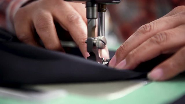 Close up seamstress using sewing machine stiching fabric together to create clothing.