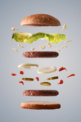 Double hamburger floating with lettuce onion and pickles gray background © Davizro Photography